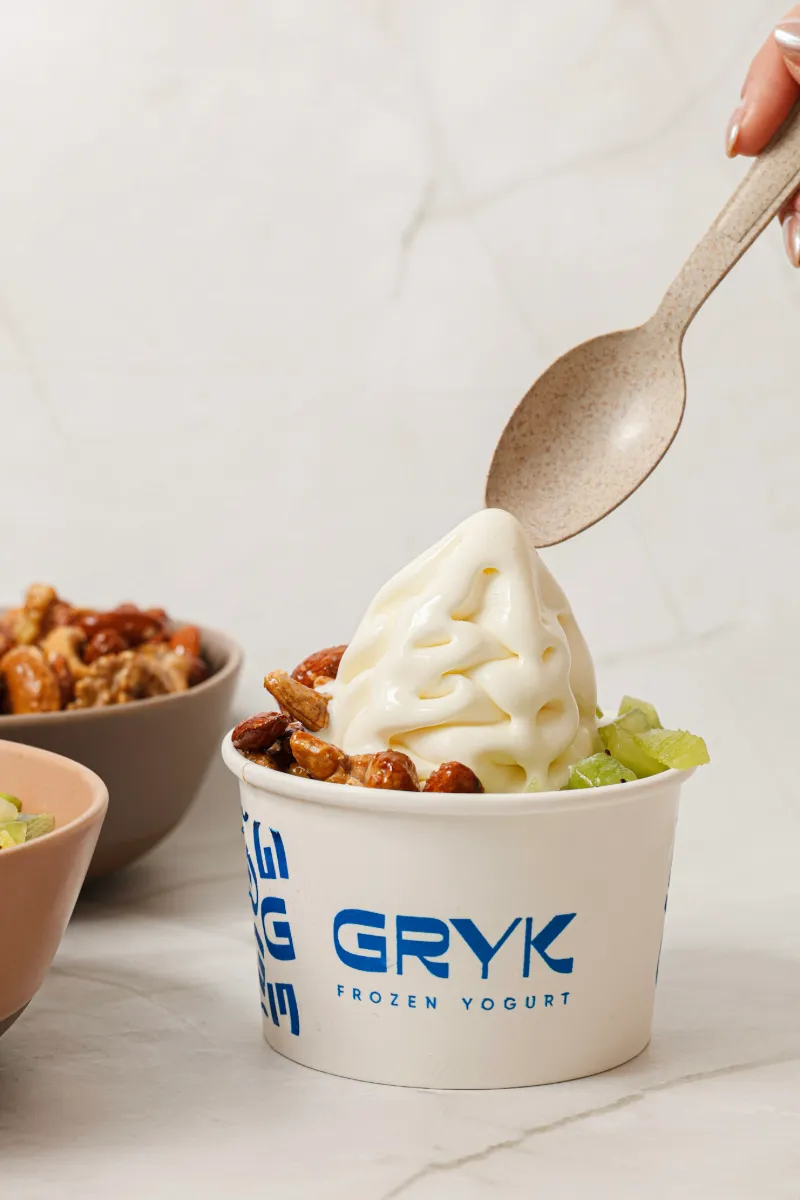 Frozen GRYK con kiwi y frutos secos caramelizados; una cuchara levanta el primer bocado